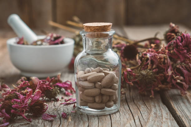 Bottle of herbal pills, mortar of healthy echinacea herbs and dry coneflower bunch on wooden table. stock photo