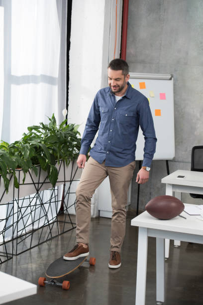 istock cheerful handsome businessman putting leg on longboard in office 1073952400