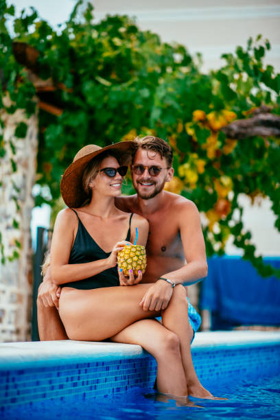 istock Young couple drinking pineapple cocktail in a pool 1073977314