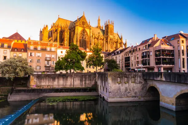 Majestic gothic cathedral of Metz on Moselle river flowing through Metz, with reflections in the water and beautiful sunset sky. France.