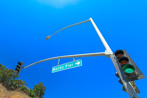 Bottom view of green Traffic Light and Malibu Pier Sign in the sunny day with blue sky. Malibu Pier is a historic landmark in California, on the Pacific Coast Highway, United States. Copy space.