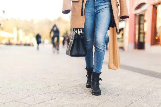 A girl walking through city in boots wearing bags.