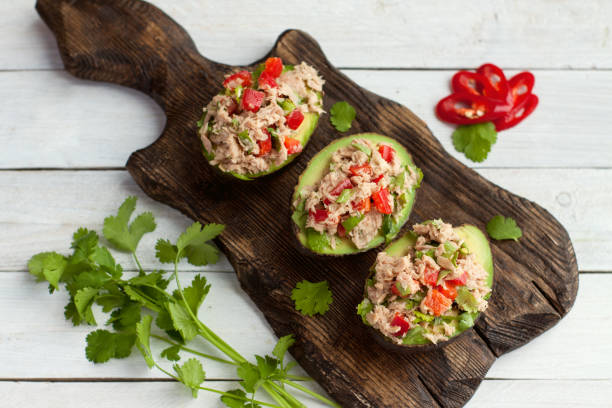 Avocados stuffed with canned tuna and vegetables Avocado appetizers stuffed with canned tuna, bell pepper, herbs on wooden cutting board stuffed stock pictures, royalty-free photos & images