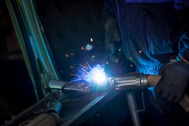 istock Male worker wearing protective gloves while repairing car exhaust pipe with welding machine 1074032994