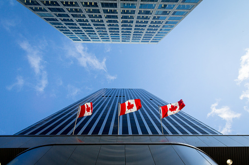 Picture of the canadian flag taken in front of a cold and blue business building in the CDB of Ottaawa. Ottawa is the capital city of Canada, and a major hub for economy, politics and business in America.