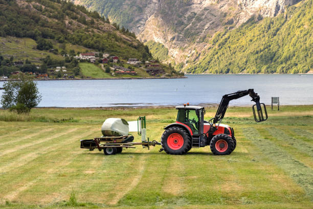 Small tractor with a round bale wrapper on a field in Geiranger, Norway. stock photo