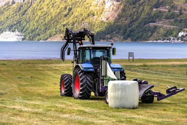 Small tractor with a round bale wrapper on a field in Geiranger, Norway.