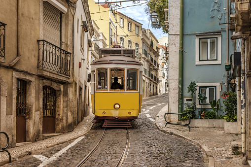 A typical vintage style public transport tram on the winding tracks in a narrow cobblestone street in Lisbon, Portugal.