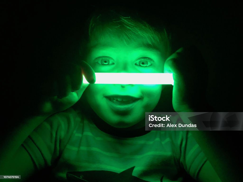 Smiling boy with glow stick, dark background Smiling boy illuminated by green glow stick against a dark background Glow Stick Stock Photo
