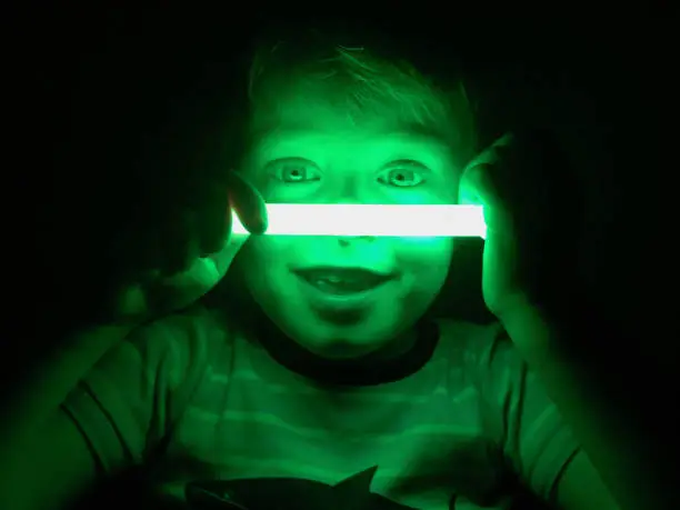 Smiling boy illuminated by green glow stick against a dark background