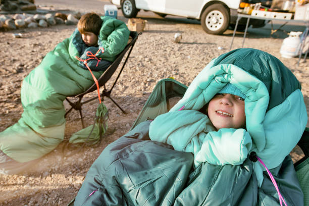 Bundled children sit in sleeping bags while camping Family with four children car camps over Mono Lake in California in late autumn. Early morning children stay in sleeping bags watching the sunrise over the lake in camp chairs. Winter clothing for the cold morning air. Mono Lake stock pictures, royalty-free photos & images