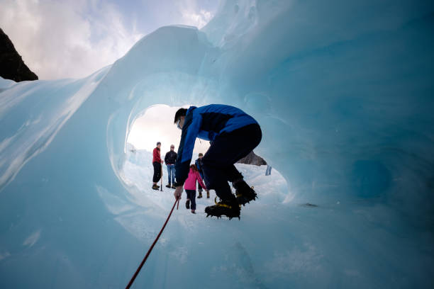 Travel adventure image of an explorer entering ice arch NEW ZEALAND, FOX GLACIER - MAY 2016: An unidentified tourist hikes through a hold at fox glacier, New Zealand. This glacier is one of the most famous attraction among tourist, traveler in New Zealand. franz josef glacier photos stock pictures, royalty-free photos & images