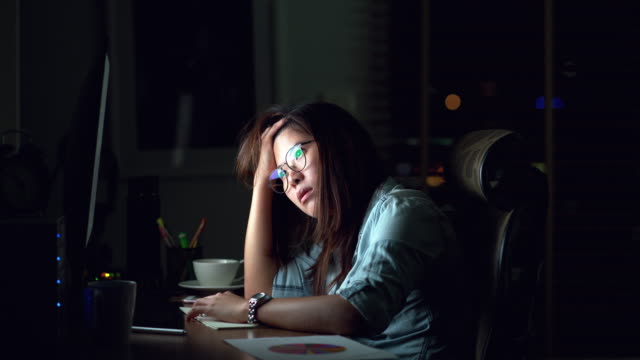遅くまで働き、暗闇の中で職場のコンピュータモニターデスクトップの前でテーブルの上で真剣な行動を考える魅力的なアジアの女性の映像シーン、仕事の後半と仕事ハードコンセプト、4kクリップ