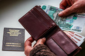 Woman's hands holding wallet with russian rubles, russian pension certificate in background.