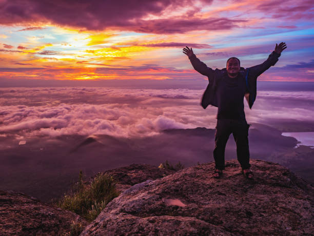 traveler stand on rocky cilff with sunsire sky and beautiful cloud sea on "pa na rai" khao luang mountian ramkhamhaeng national park - rocky mountian imagens e fotografias de stock