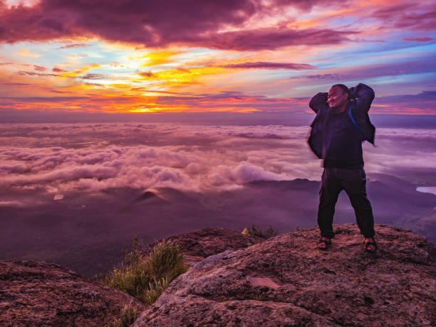 traveler stand on rocky cilff with sunsire sky and beautiful cloud sea on "pa na rai" khao luang mountian ramkhamhaeng national park - rocky mountian imagens e fotografias de stock