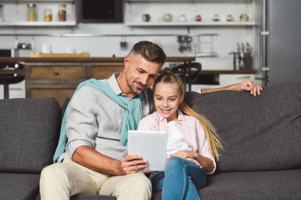 istock father and daughter sitting on sofa and using digital tablet 1074143168