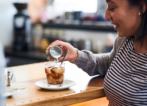 Shot of a woman pouring milk into her coffee in a coffee shop