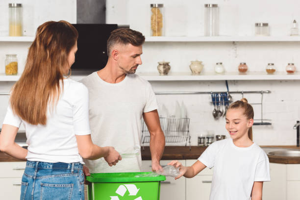 istock family standing at kitchen and putting empty plastic bottles in green recycle box 1074145886