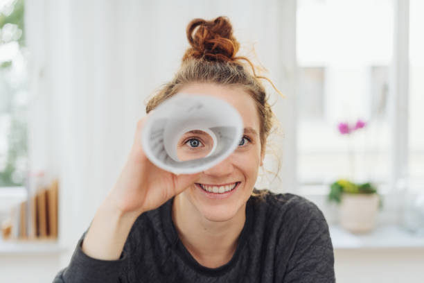 Young woman playing I spy with the camera Young woman playing I spy with the camera looking through a rolled cylinder of paper with one eye and a happy smile searching stock pictures, royalty-free photos & images
