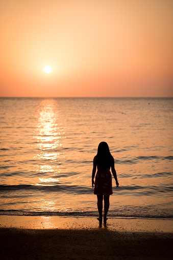 Image silhouette of young lady walking on the sunset beach.