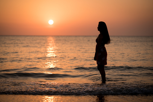 Image silhouette of young lady walking on the sunset beach.