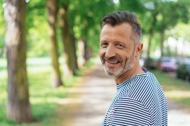 Cheerful mature man standing in park Portrait of smiling mature man standing in park on sunny day german people stock pictures, royalty-free photos & images