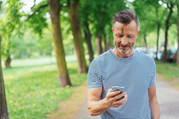 Man dialling a call on his mobile phone Man dialling a call on his mobile phone as he stands in a shady tree line road in a park dialling phone stock pictures, royalty-free photos & images