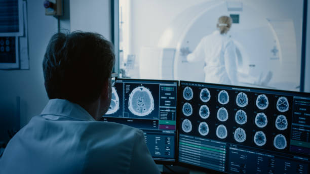 In Medical Laboratory Patient Undergoes MRI or CT Scan Process under Supervision of Radiologist, in Control Room Doctor Watches Procedure and Monitors with Brain Scans Results. In Medical Laboratory Patient Undergoes MRI or CT Scan Process under Supervision of Radiologist, in Control Room Doctor Watches Procedure and Monitors with Brain Scans Results. radiologist photos stock pictures, royalty-free photos & images