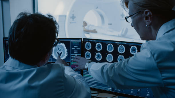istock In Control Room Doctor and Radiologist Discuss Diagnosis while Watching Procedure and Monitors Showing Brain Scans Results, In the Background Patient Undergoes MRI or CT Scan Procedure. 1074166410