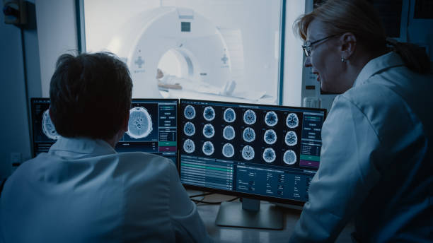 istock In Control Room Doctor and Radiologist Discuss Diagnosis while Watching Procedure and Monitors Showing Brain Scans Results, In the Background Patient Undergoes MRI or CT Scan Procedure. 1074166412