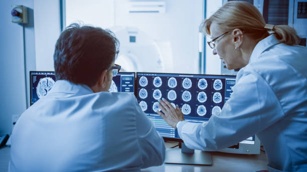 istock In Control Room Doctor and Radiologist Discuss Diagnosis while Watching Procedure and Monitors Showing Brain Scans Results, In the Background Patient Undergoes MRI or CT Scan Procedure. 1074166442