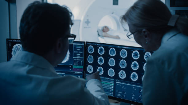 istock In Control Room Doctor and Radiologist Discuss Diagnosis while Watching Procedure and Monitors Showing Brain Scans Results, In the Background Patient Undergoes MRI or CT Scan Procedure. 1074166468