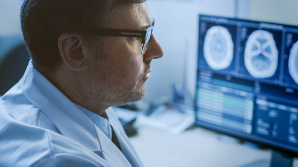 ritratto ravvicinato del medico professionista che guarda le immagini della risonanza magnetica o della tac sul suo monitor del computer, alla ricerca di segni di tumore al cervello o cancro, cercando di diagnosticare la malattia. - radiologist computer doctor mri scan foto e immagini stock