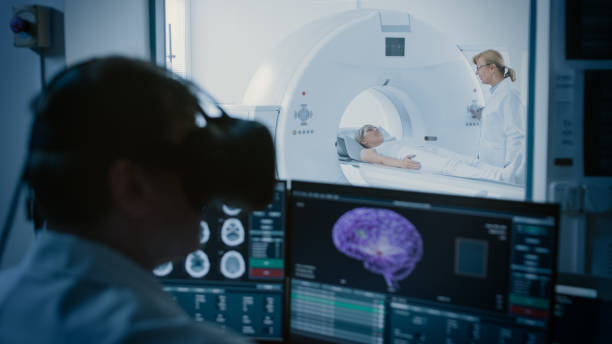 futurystyczna koncepcja: w pokoju kontroli medycznej lekarz noszenia zestawu słuchawkowego wirtualnej rzeczywistości monitoruje pacjenta poddawanego procedurze mri lub ct scan. wyświetlacze komputerowe pokaż model mózgu 3d z możliwym rakiem. - mri scan obrazy zdjęcia i obrazy z banku zdjęć