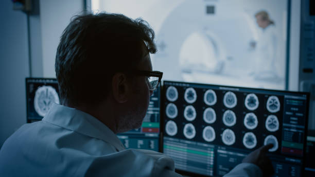 istock In Medical Laboratory Patient Undergoes MRI or CT Scan Process under Supervision of Radiologist, in Control Room Doctor Watches Procedure and Monitors with Brain Scans Results. 1074166574