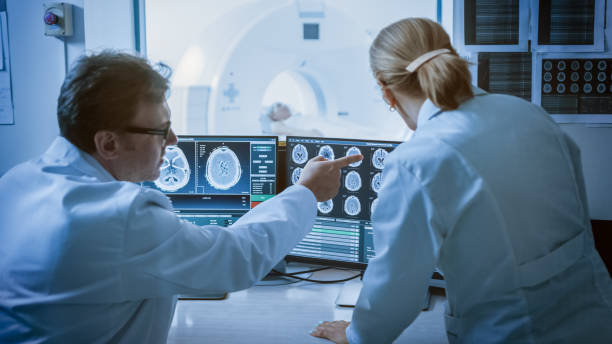 nella sala di controllo medico e radiologo discutono della diagnosi durante la procedura di osservazione e monitorano la visualizzazione dei risultati delle scansioni cerebrali, nel paziente in background viene sottoposto a risonanza magnetica o procedura  - radiologist computer doctor mri scan foto e immagini stock