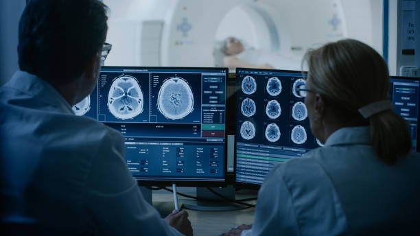 istock In Control Room Doctor and Radiologist Discuss Diagnosis while Watching Procedure and Monitors Showing Brain Scans Results, In the Background Patient Undergoes MRI or CT Scan Procedure. 1074166724
