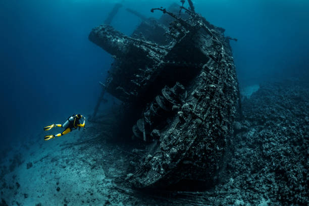 Scuba diver observing a large shipwreck completely rusted and overgrown lying underwater in the Red Sea Scuba diver passing by a wreckage of a large sunken ship in the Red Sea. sunken stock pictures, royalty-free photos & images