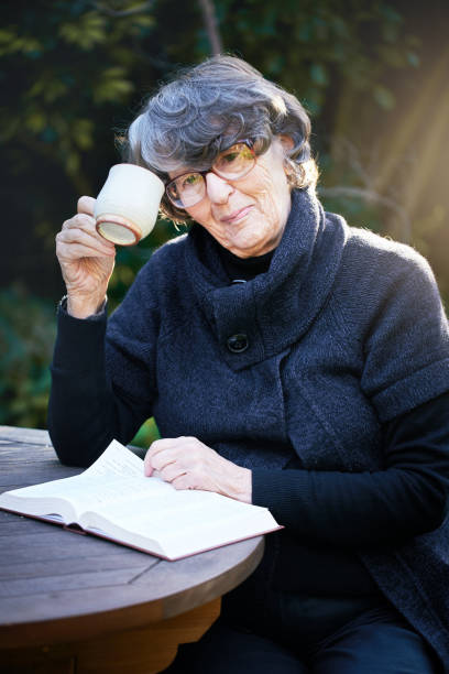 istock Senior woman outdoors smiles, drinking coffee as she reads book 1074174128