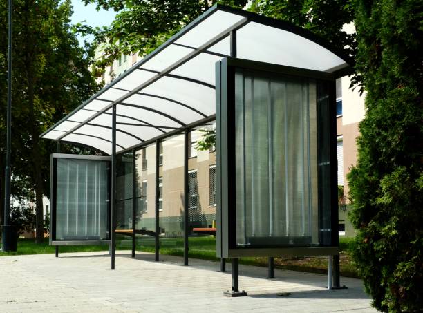 modern glass bus shelter in urban setting modern designed transparent glass bus shelter in urban setting with residential building and green park in the background bus shelter stock pictures, royalty-free photos & images