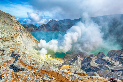 The green crater lake of the Ijen volcano in East Java, Indonesia. At the shore of the acid lake there is an active vent which is a source of elemental sulfur. At this place local people do sulfur mining - the miners break out the sulfur in large pieces and carry it in baskets up to the crater rim and afterwards down to the village at the slopes of the vulcano. These workers are carrying baskets with loads between 70 and 100 kilograms, most of them are doing this twice a day.