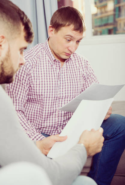 istock Upset man with friend looking at papers on sofa 1074205518