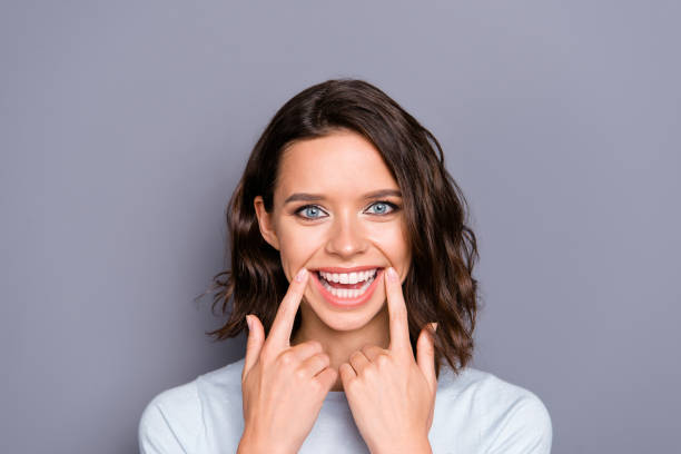 Close up photo portrait of cheerful glad positive lady with her Close up photo portrait of cheerful glad positive lady with her brunette hair she demonstrate toothy wide hollywood smile isolated on gray background hold forefingers on two hand near mouth tooth whitening photos stock pictures, royalty-free photos & images