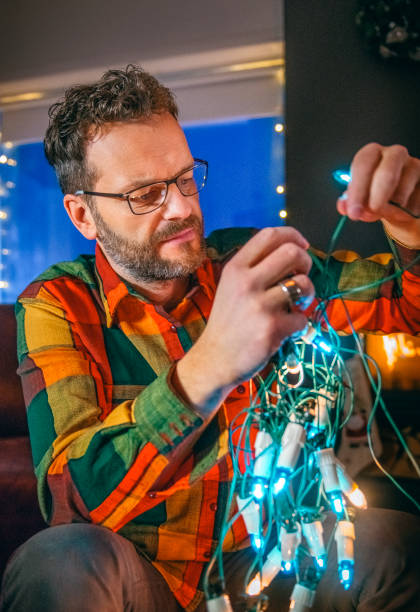 homem tentando desembaraçar as luzes de natal em casa - christmas tangled christmas lights lighting equipment - fotografias e filmes do acervo