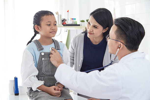 istock Professional doctor wearing white coat using stethoscope to examine kid patient with her mother in hospital background 1074219484