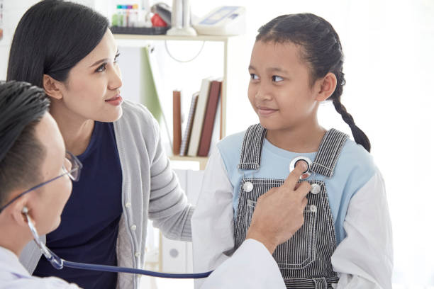 istock Professional doctor wearing white coat using stethoscope to examine kid patient with her mother in hospital background 1074219552