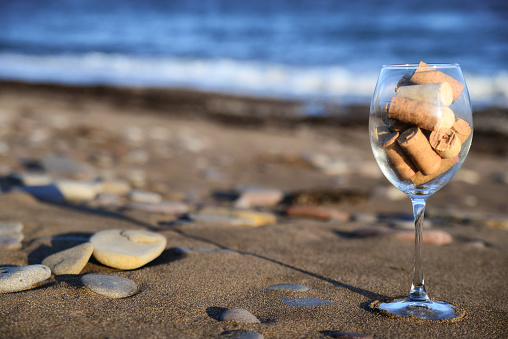 Large wine glass filled with cork stoppers stands on a sandy beach against the sea