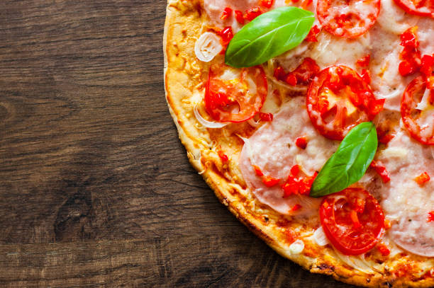 istock sliced Pizza with Mozzarella cheese, Ham, Tomatoes, pepper, Spices and Fresh Basil. Italian pizza on wooden background. 1074236252