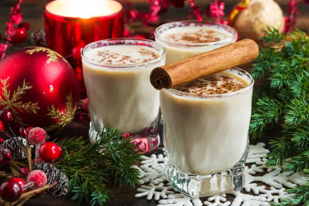 Eggnog with milk, rum, cinnamon and nutmeg in the glasses on the rustic wooden table with Christmas decoration.